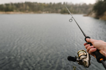 Fisherman hands with rod, spinning reel on the river bank. Man catching fish, pulling rod while...