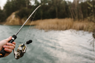 Fisherman hands with rod, spinning reel on the river bank. Man catching fish, pulling rod while fishing from lake or pond with text space. Fishing for pike, perch on lake or pond. Fishing day concept.