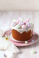 Kulich Russian Easter Cake with raisins, topped with icing glaze and decorated with colored meringue cookies, on white wooden table.