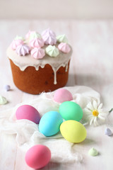 Kulich Russian Easter Cake with raisins, topped with icing glaze and decorated with colored meringue cookies, on white wooden table.