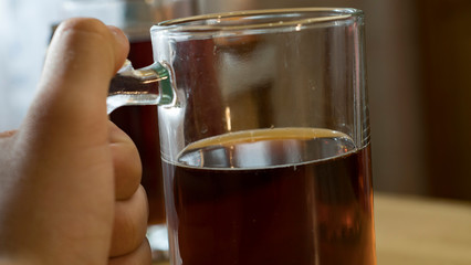 Glass mug with dark beer in a man's hand