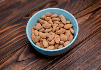 Raw almonds nuts in a bowl on a wooden background. Healthy fat food