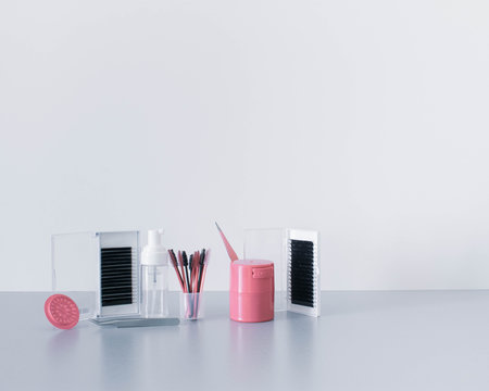 Cool, glamorous and sophisticated beauty background or backdrop with lash extension treatment products, tools and equipment standing against a crisp white background on top of a cool grey surface