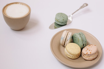Homemade colorful macarons on the brown plate on the white background. Cup of coffee. Blossom.