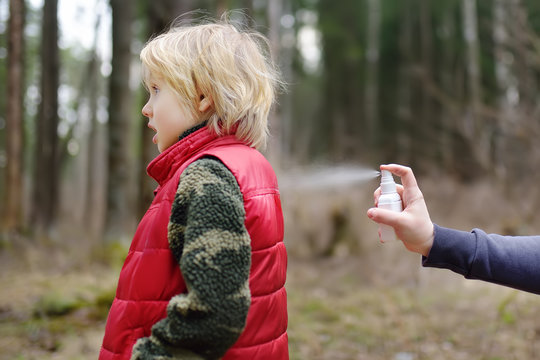 Woman spraying ticks bite repellents on little boy during a walk in the forest. Protect children from dangerous insects while hiking.