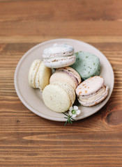 Colorful homemade macarons are lying on the beige plate on the brown wooden background. Pattern.