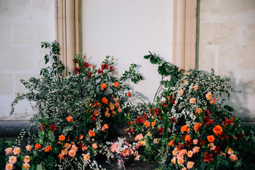 the unusual area of the wedding venue on the background of the wall with stucco is decorated with fresh flowers in the form of thickets and the main color accent coral