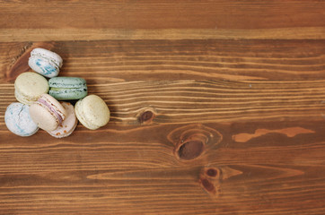 Colorful homemade macarons are lying on the brown wooden background. Pattern.