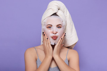 Horizontal picture of good looking magnetic female putting hands on face, having face mask, caring...