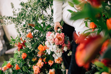 a bouquet in the hands of the bride shot between floral arrangements of fresh flowers in color coral created for a wedding ceremony