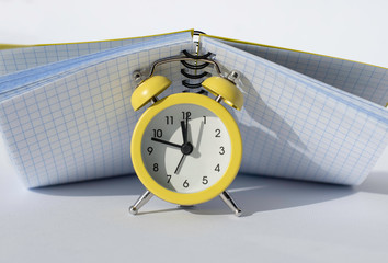 Yellow alarm clock covered by notebook.Time management concept . Educational concept.