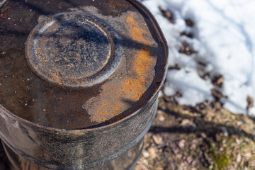 inverted rusty barrel made of metal for water, in the spring against the backdrop of snow.