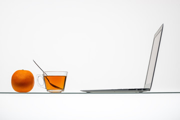 orange with tea cup and laptop on inclined glass table surface 