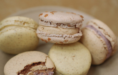 Yellow homemade macarons with blossom are lying on the brown plate on the golden background.
