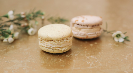 Two homemade macarons with blossom are lying on the golden background.