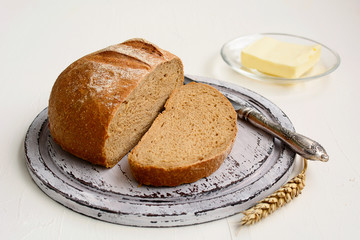 Rye bread, butter and knife on a wooden plate on a white background