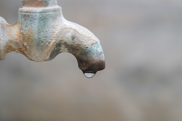 Water that is dripping from the vintage old brass faucet with blurred cement wall background close-up.