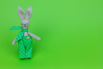 Rabbit in green pants with a bow on his neck. Green background Free space for text. Handmade toy....