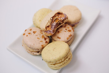 Yellow homemade macarons with blossom are lying on the white plate on the white background.