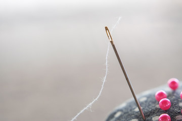 Needle with thread and pink pins on pincushion for handmade sewing cloth with blurred background...