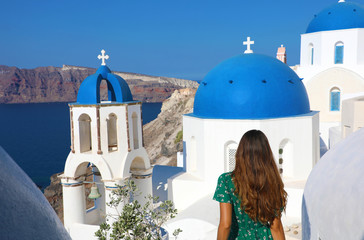 Tourism in Greece. Back view of traveler tourist girl visiting the famous white village with blue domes of Oia, Santorini. European travel destination.