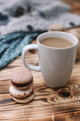 Two homemade colorful macaroons are lying on the brown wooden table with cup of coffee. Cup of coffee. Colorful tissue.