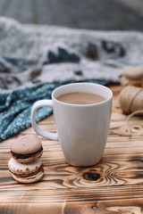 Two homemade colorful macaroons are lying on the brown wooden table with cup of coffee. Cup of coffee. Colorful tissue.