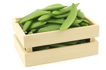 freshly harvested sugar snaps in a wooden box on a white background