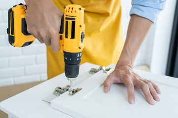 close up man holding cordless screwdriver machine and screws lie for screwing a screw assembling furniture at home.