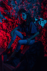 haute couture with pink blue neon hair. Young beautiful woman model, fashionable glowing hairstyle, makeup. Stylish Art Studio Portrait. Colorful Bright Light. black coat, newspaper background