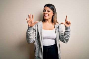 Young beautiful brunette sportswoman wearing sportswoman training over white background showing and pointing up with fingers number seven while smiling confident and happy.