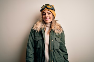 Young brunette skier woman wearing snow clothes and ski goggles over white background with a happy and cool smile on face. Lucky person.