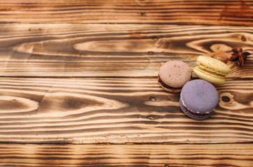 Three homemade colorful macaroons are lying on the brown wooden table with cup of coffee with the place for text. Colors.