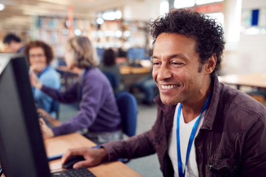 Group Of Mature Adult Students In Class Working At Computers In College Library