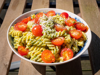Fusilli Pasta with pesto, chopped cherry tomatoes and grated parmesan cheese. Placed on a wooden table outdoors. 