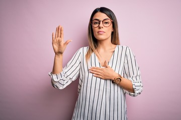 Young beautiful woman wearing casual striped t-shirt and glasses over pink background Swearing with...