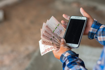 The hands of the construction workers holding banknotes and mobile phones
