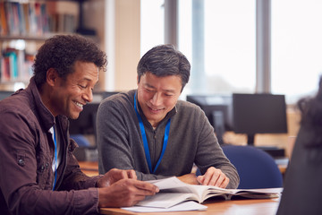 Teacher With Mature Male Adult Student Sitting At Table Working In College Library