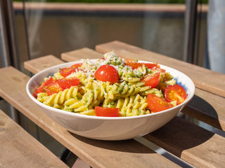 Fusilli Pasta with pesto, chopped cherry tomatoes and grated parmesan cheese. Placed on a wooden table outdoors. 