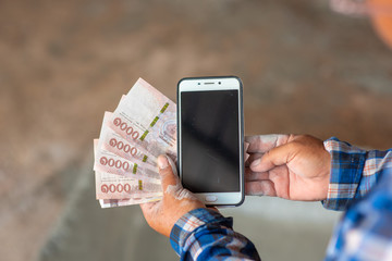The hands of the construction workers holding banknotes and mobile phones