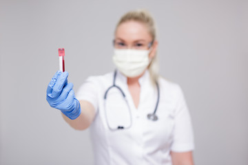 health care, medicine, microbiology and corona virus pandemic concept - doctor or nurse in white uniform and medical mask holding blood test tube