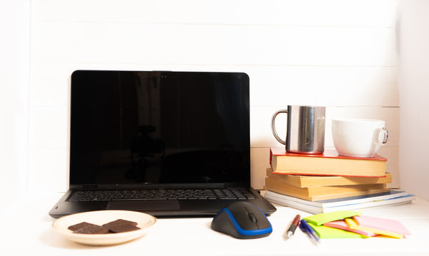 Home office concept. Work from home. Black laptop, books and cafe cuo on the white wooden background. Side view. Sweden. Stockholm.