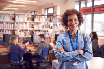 Portrait Of Mature Female Teacher Or Student In Library With Other Students Studying In Background