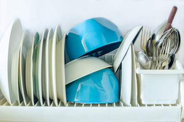 White and blue plates for eating, cutlery forks, knives, spoons in a glass for drying dishes in the kitchen on a white background.