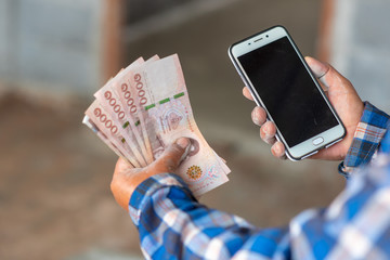 The hands of the construction workers holding banknotes and mobile phones