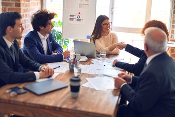 Group of business workers smiling happy and confident in a meeting. Speaking with smile on face working together shaking hands for agreement at the office.