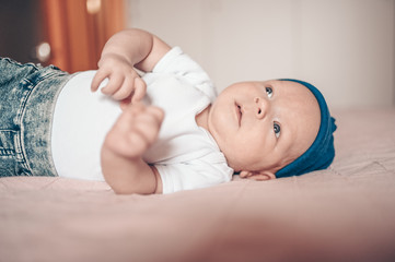 Cute little baby boy lying on pink blanket at bedroom. Newborn. Baby stays awake on the bed. Closeup portrait of emotional newborn baby in blue jeans and white t-shirt