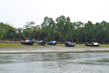 Different sized fishing boats ported on a small bank of a river side while the river is full of water