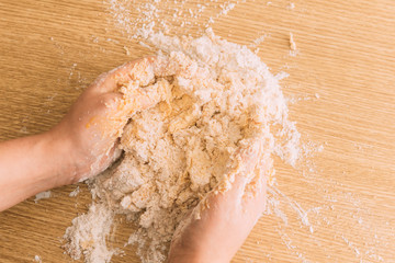 Vista cenital de dos manos amasando harina para hacer galletas, fondo rústico de madera, cálido