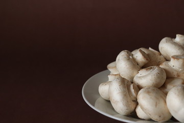 raw mushrooms on a plate on dark brown background